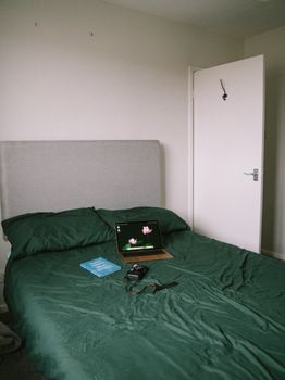 A comfortable bedroom features a green bedspread, laptop, camera, and a book, capturing a tech-savvy vibe.