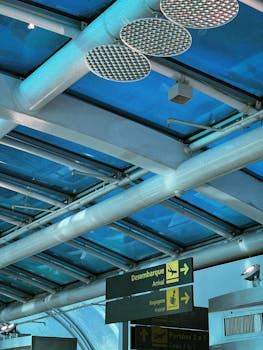 A modern airport terminal with blue glass roof and directional signs for arrivals in multiple languages.
