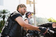 明媚的阳光下，两名穿着皮背心的男子骑着摩托车