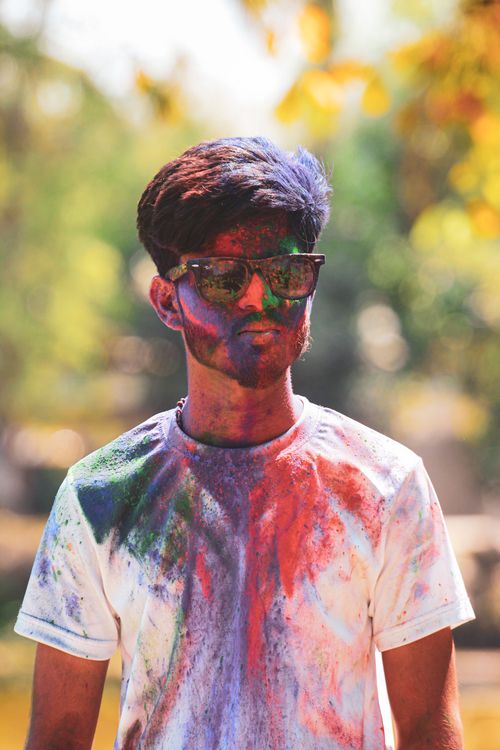 Free Young man with vibrant face paint outdoors, celebrating Holi festival with colored powders. Stock Photo