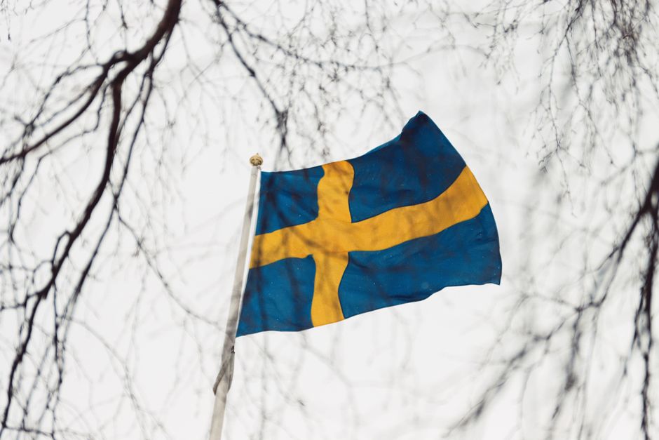 Swedish flag waving on a flagpole amongst bare branches in Jönköping, Sweden.