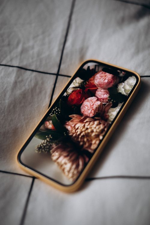 Free A smartphone displays a vivid flower reflection on a bed, creating a cozy visual. Stock Photo