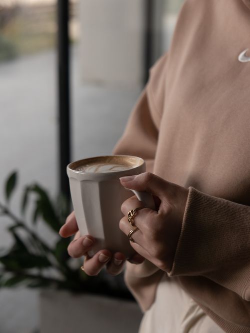 Free Cozy indoor shot of a woman holding a steaming coffee mug with rings visible. Stock Photo