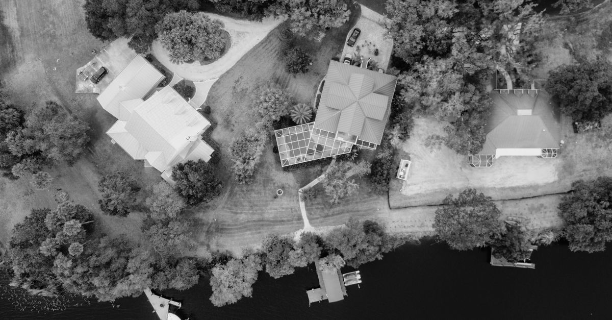 Black and white aerial shot showcasing riverside homes with a dock area surrounded by lush trees.