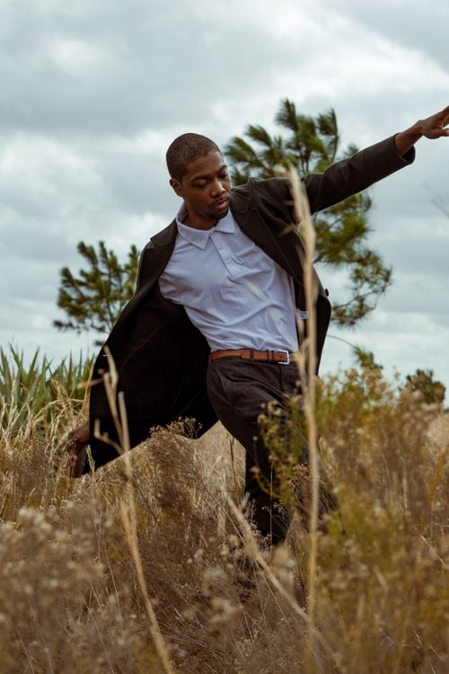 Free A fashionable man in a suit jacket poses dynamically in a natural field setting. Stock Photo