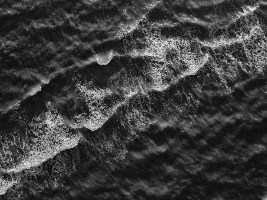 A striking aerial view of ocean waves in black and white, capturing the dynamic motion and textures of the sea.