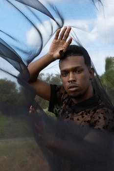 Artistic portrait of a man posing with a flowing black veil outdoors, exuding fashion and elegance.