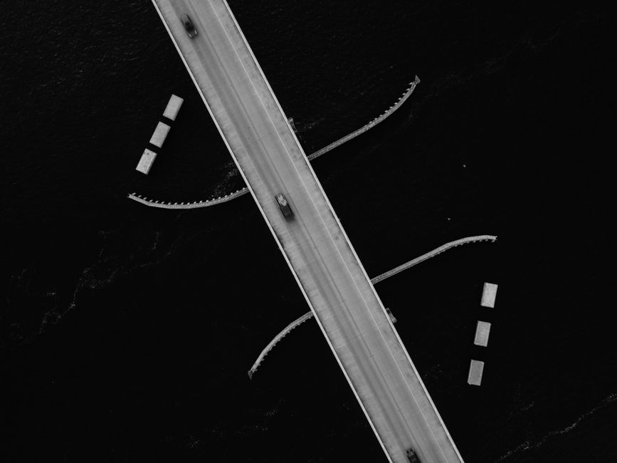 Black and white aerial photo of a bridge over water, showcasing transport infrastructure.