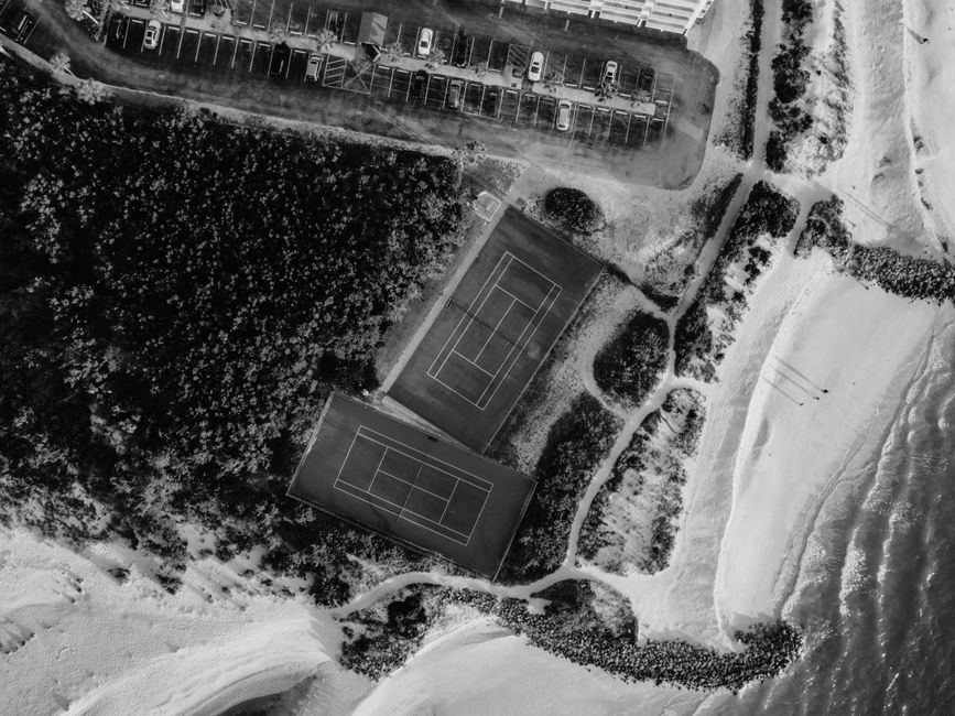 Aerial view of tennis courts near a beach, captured in black and white.