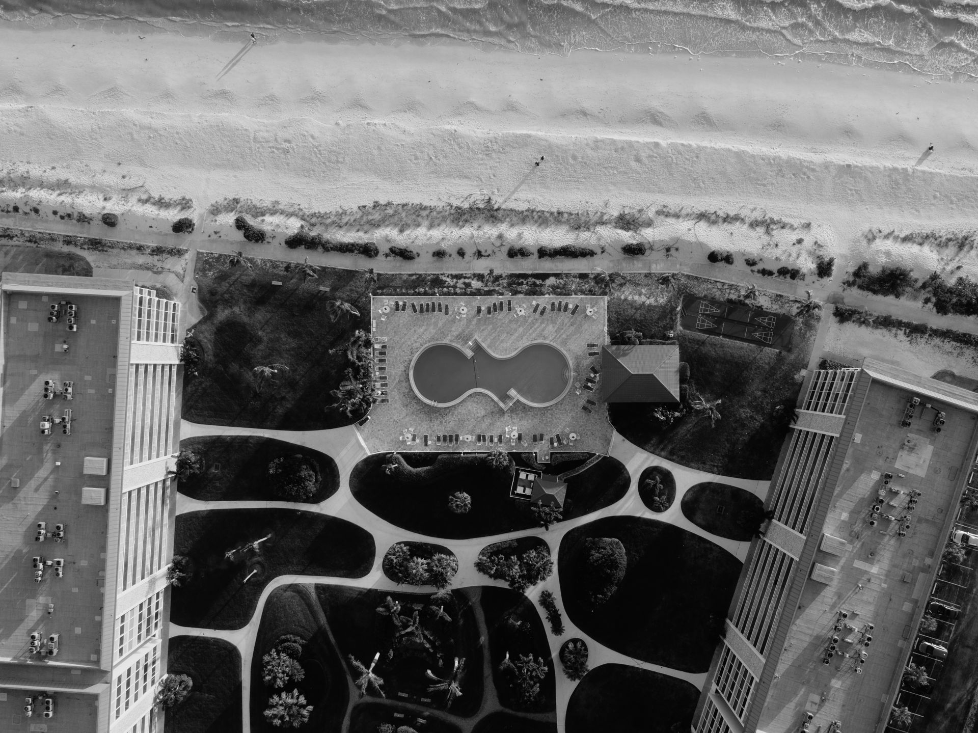 Black and white aerial shot of a beachfront resort with an infinity pool and beach access.