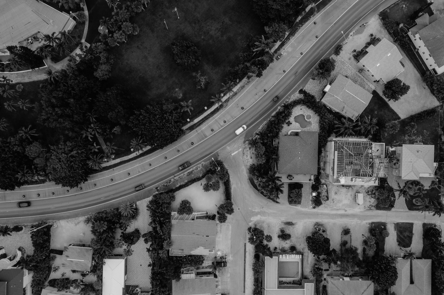 Black and white aerial photo of a residential neighborhood with a curving roadway and vehicles.