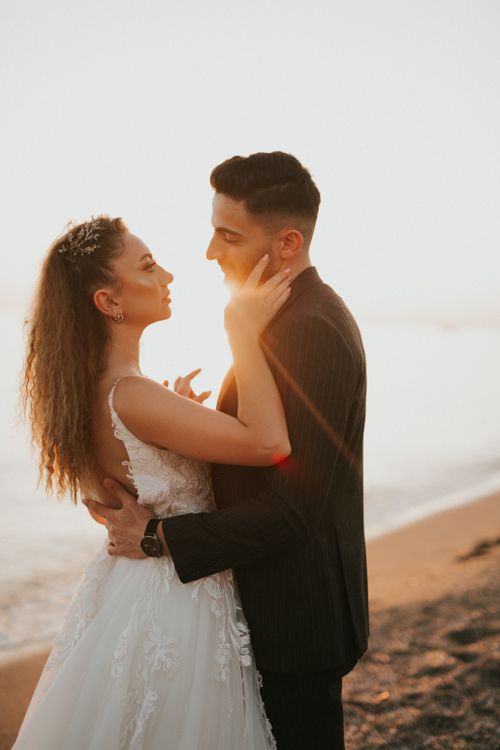 Free A wedding couple embraces on a beach with the setting sun in the background. Stock Photo
