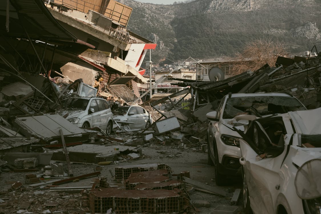 Collapsed buildings and crushed cars after devastating earthquake in mountainous urban area.