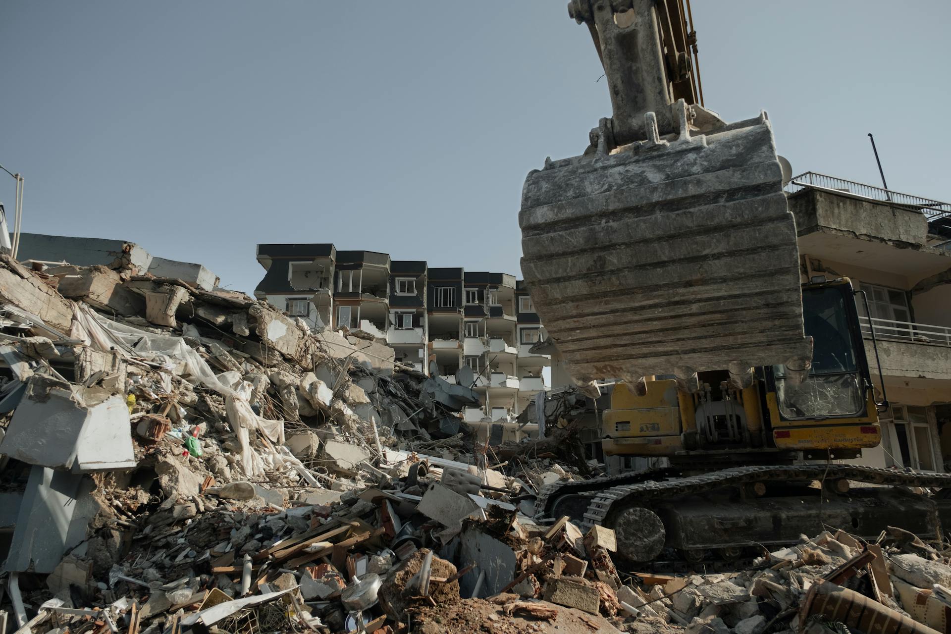 Powerful excavator clearing earthquake debris amidst building ruins in Antakya, Turkey.