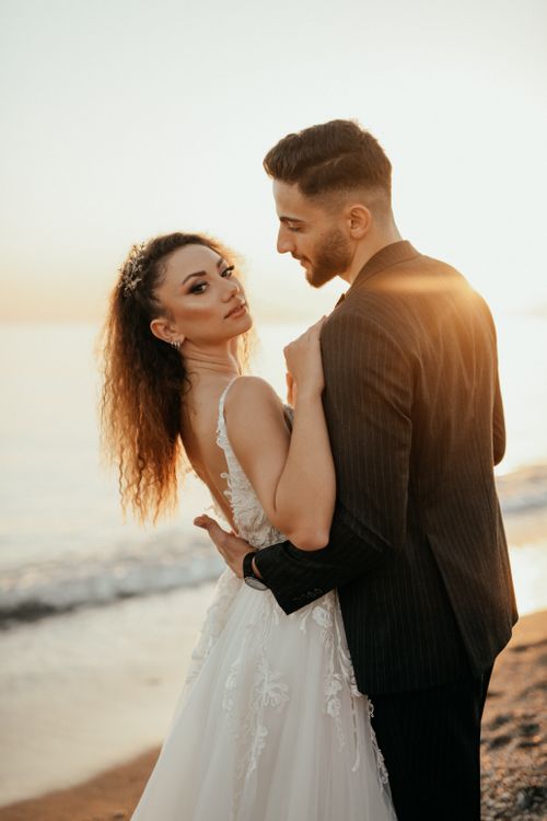 Free Bride and groom embracing on a sunlit beach during their wedding at sunset. Stock Photo