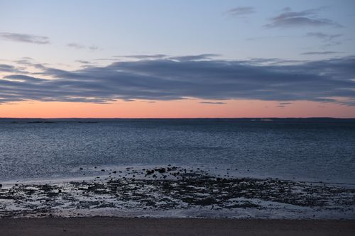 Free Tranquil beach scene at dusk with serene ocean waves and vibrant sunset colors. Stock Photo