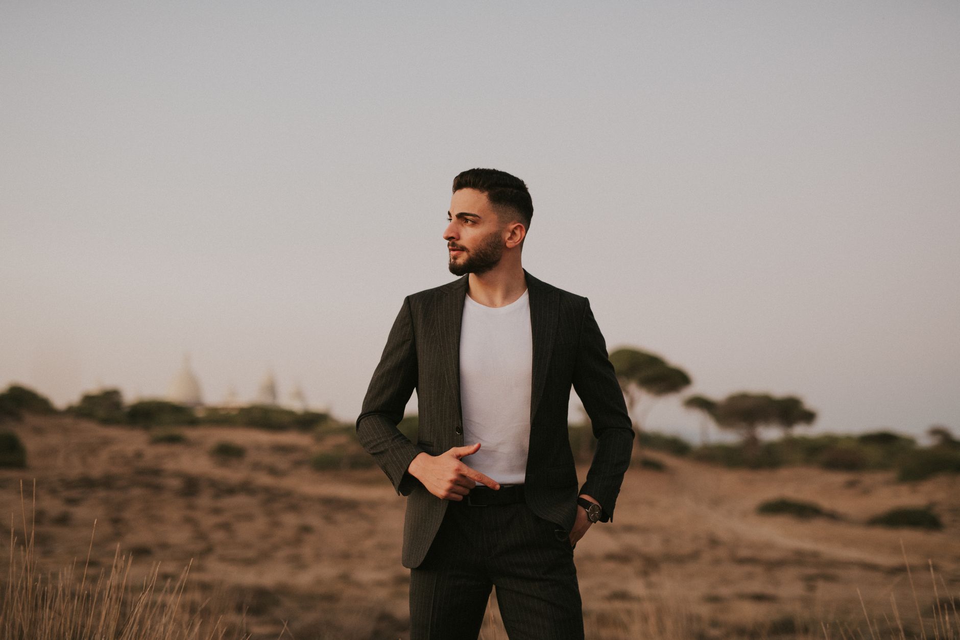 Man in suit posing confidently in a serene desert landscape at dusk.