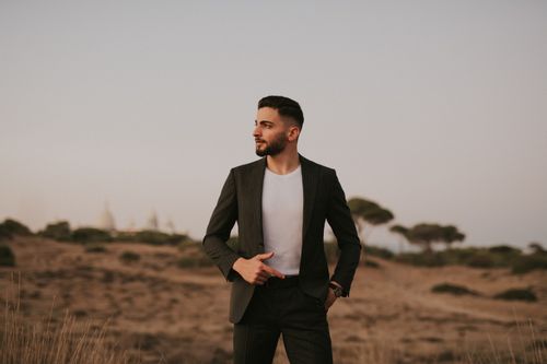 Free Man in suit posing confidently in a serene desert landscape at dusk. Stock Photo