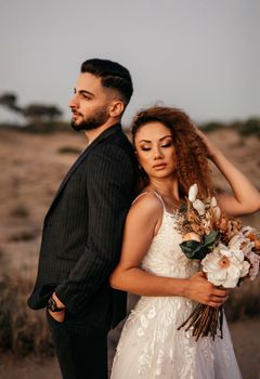 A couple posing in wedding attire on a beach during sunset, exuding romance.