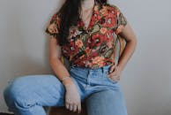 一位时尚女士穿着充满活力的花卉衬衫和牛仔裤，随意地坐在室内