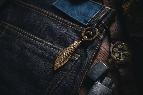Free Close-up view of a detailed brass fish-shaped keychain attached to stylish denim jeans. Stock Photo