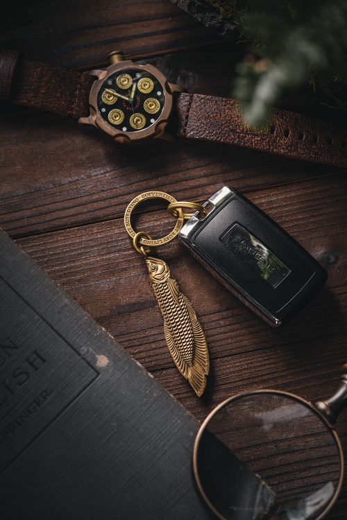 Free Close-up of a brass fish-shaped keychain lying on a wooden surface beside a bullet watch and magnifying glass. Stock Photo