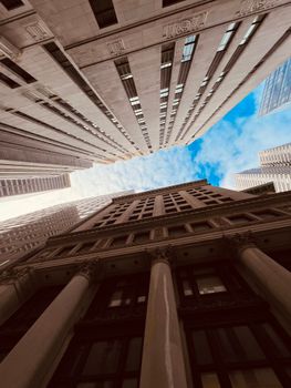 Dramatic view looking up at skyscrapers against a blue sky in an urban setting.