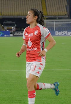 Woman running on football field during a game, wearing team uniform.