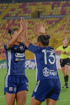 Two female soccer players celebrating a goal during a match in a vibrant stadium.
