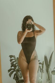 Artistic mirror selfie of a woman in a black swimsuit indoors, capturing a natural and expressive moment.