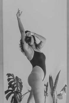 Elegant black and white photo of a woman posing with a camera, surrounded by plants.