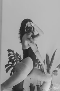 Black and white photo of a woman in a bodysuit posing with a camera.