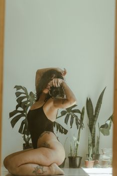 A woman poses with a camera amidst green indoor plants, exuding natural elegance.