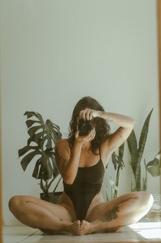 A woman sitting cross-legged capturing a mirror selfie with plants in the background.