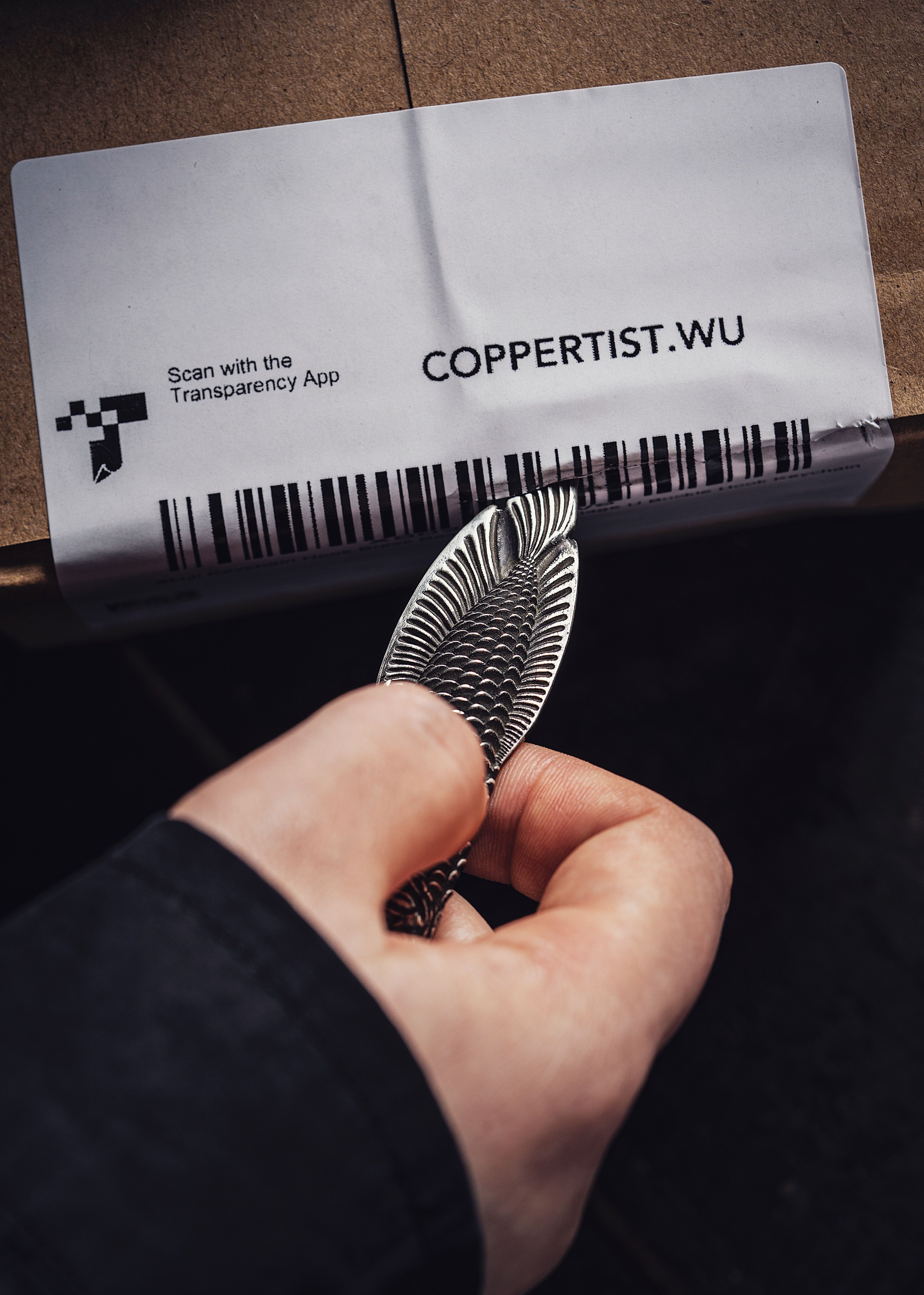 A close-up image of a hand holding a silver, fish-shaped tool above a package label.