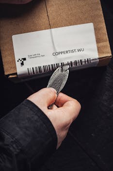 Close-up of a hand using a silver tool to open a cardboard package.