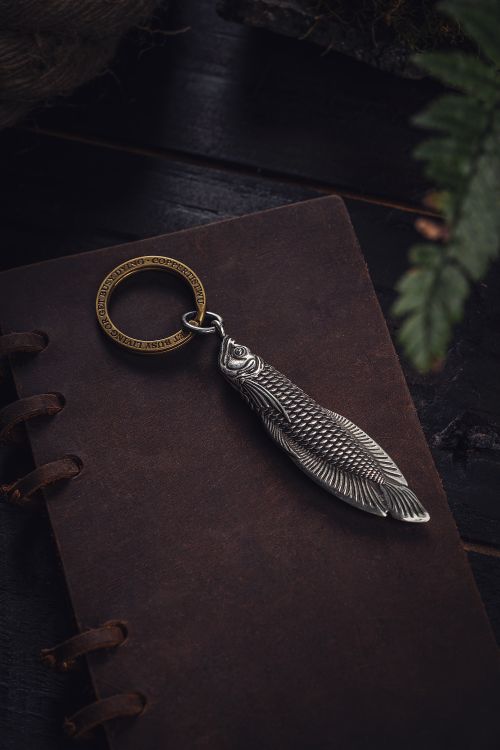 Free A vintage silver fish keychain rests on a rustic brown notepad, creating a nostalgic tone. Stock Photo