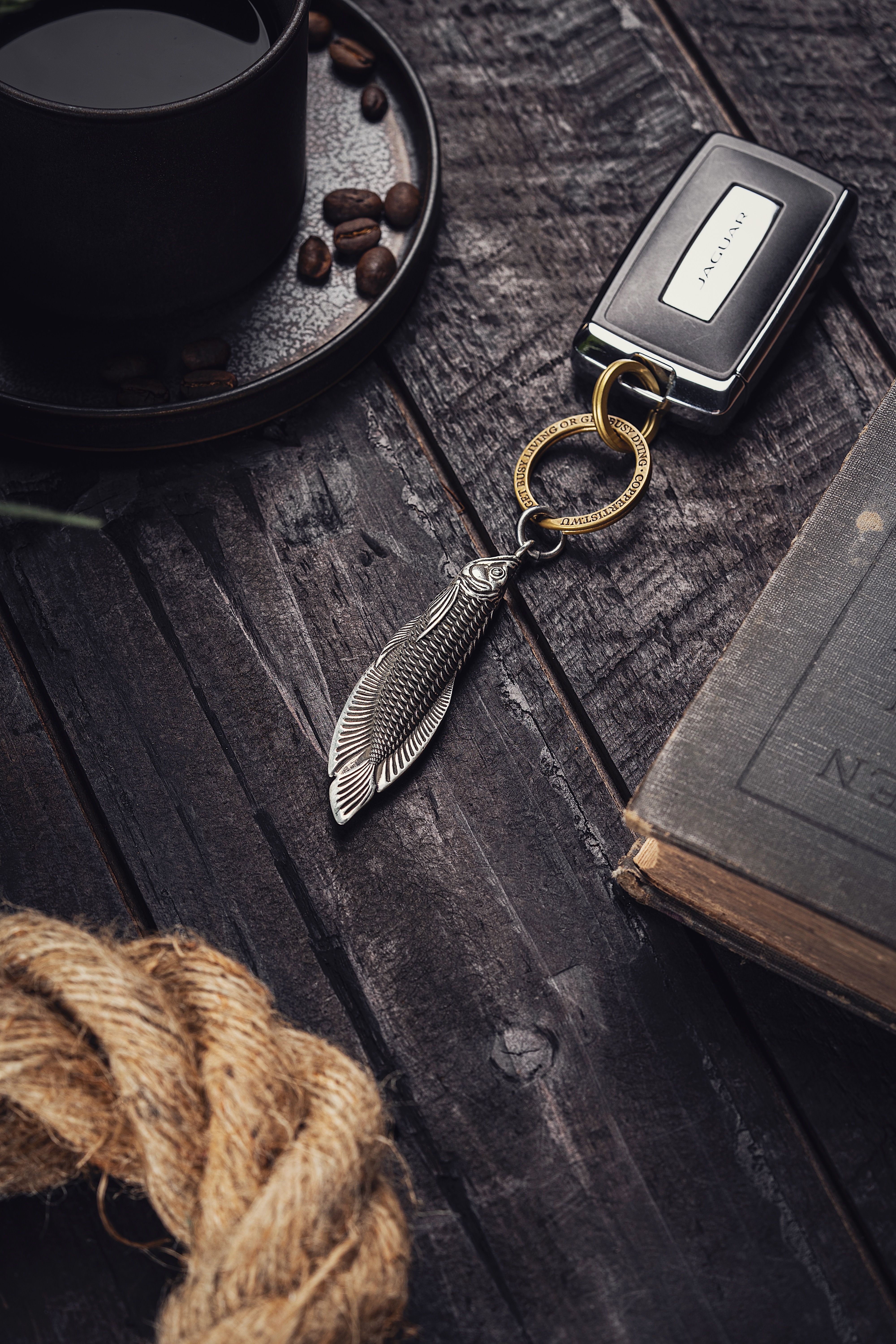 A detailed fish-shaped keychain with coffee and rope on a rustic wooden table, evoking a vintage charm.