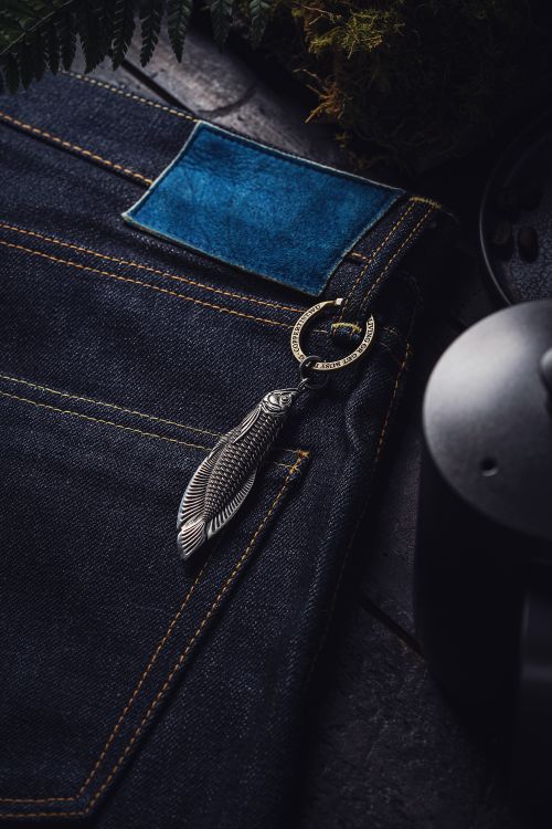 Free Artistic display of a fish-shaped steel keychain attached to jeans with a coffee pot and fern accent. Stock Photo