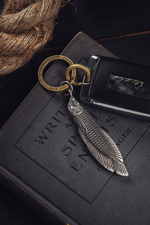 Free Stylish car key with fish-themed silver keychain on vintage book, perfect for automotive and design aesthetics. Stock Photo