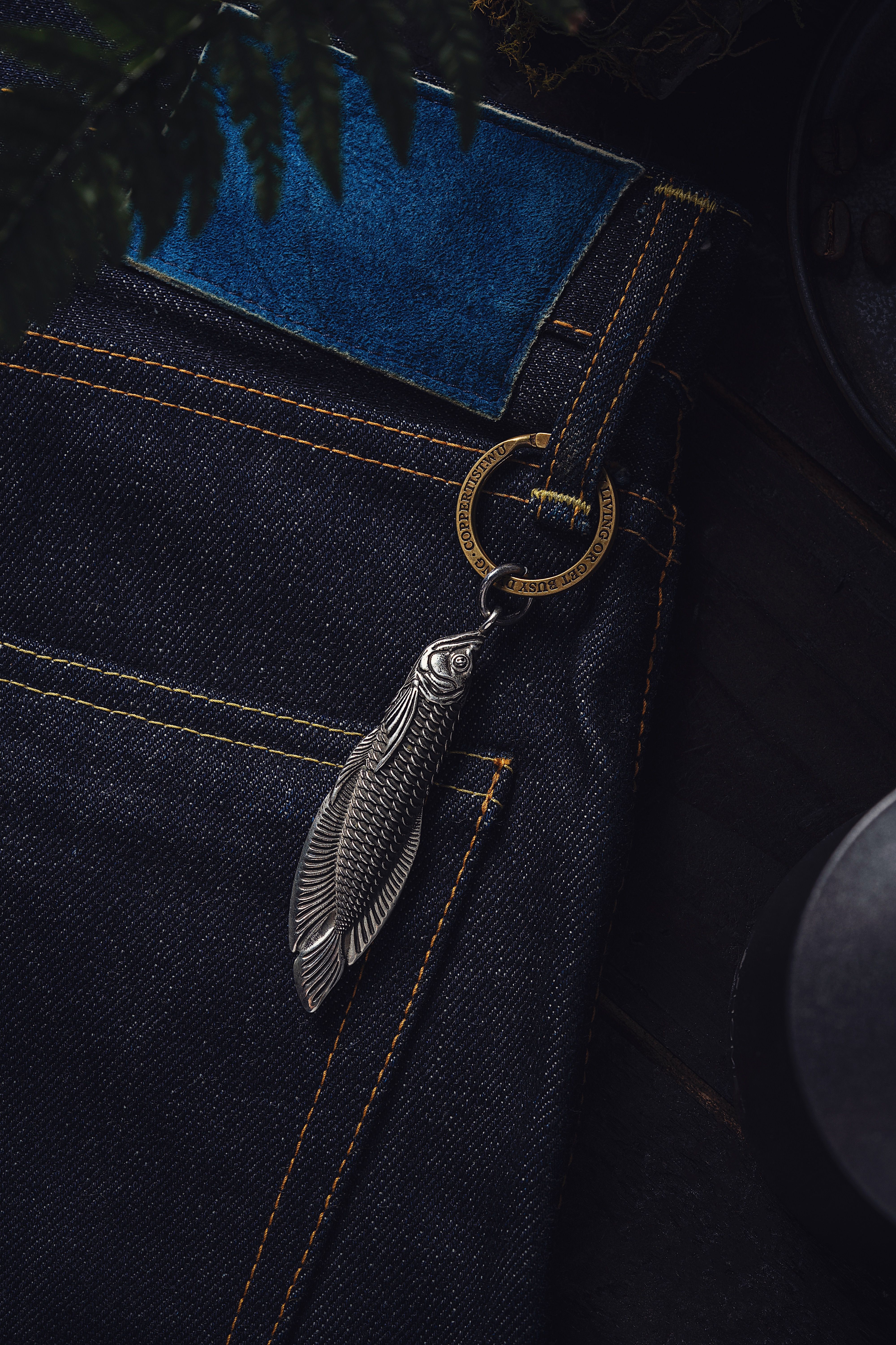 Close-up of denim jeans featuring a silver fish pendant keychain, perfect for fashion and accessories.