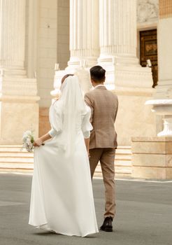 Bride and groom walking together in an elegant outdoor setting, showcasing wedding attire.