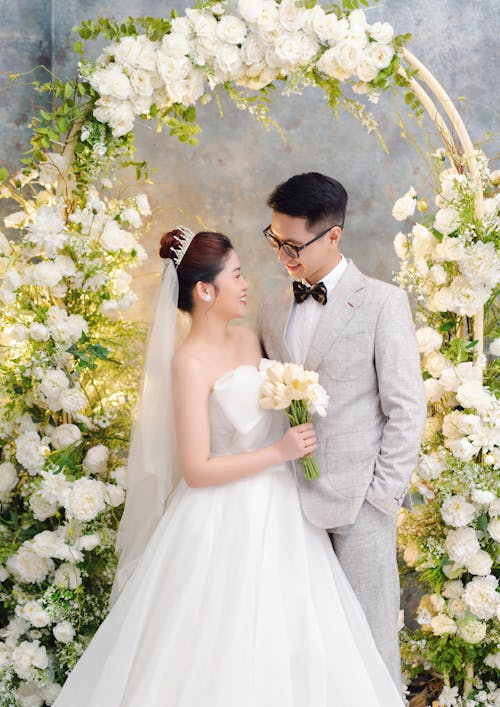 Bride and Groom Standing under an Archway Decorated with Flowers 