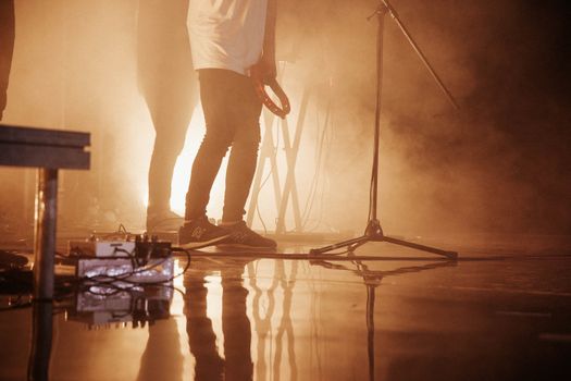 Men performing on a dramatic smokey stage with musical instruments and reflections.