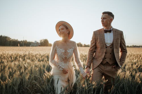 Newlyweds Holding Hands and Walking in Sunlight over Field