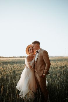A happy couple embraces in a sunlit rural field, capturing a romantic wedding moment.