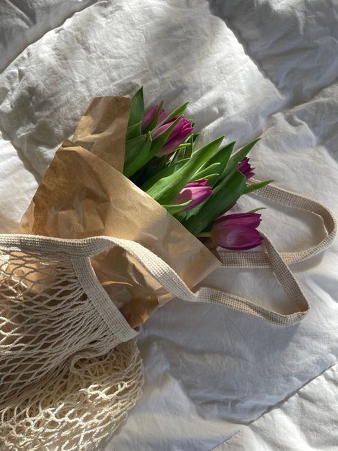 Purple tulips wrapped in paper within an eco-friendly net bag on a soft surface.