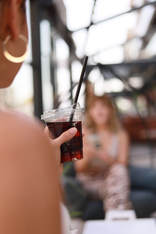 Free Close-up of a woman holding a cold drink with a straw, blurred background Stock Photo