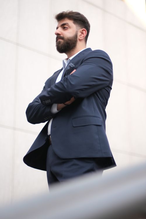 Free Stylish man with beard poses confidently with arms crossed, wearing a suit outdoors. Stock Photo