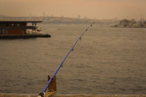Free Fishing rod overlooking a city skyline under a warm, hazy sky, capturing a peaceful moment by the water. Stock Photo